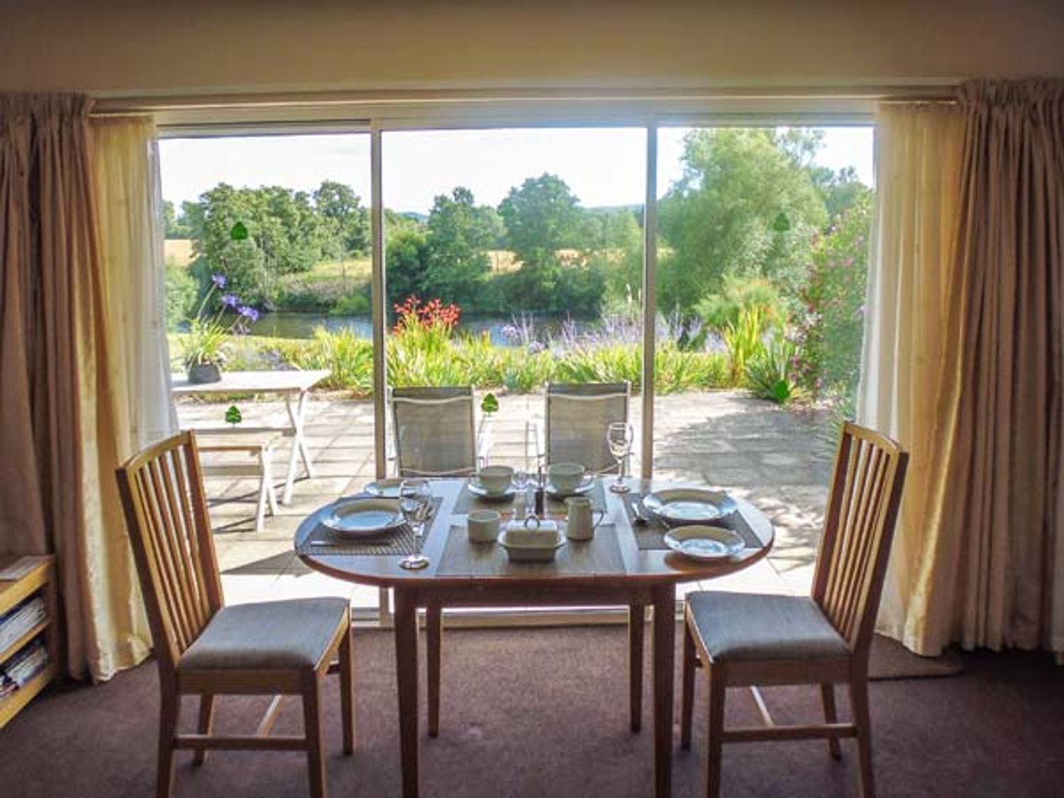 A dining area with a table set for four by a sliding glass door overlooking a garden and patio at Herons in Byford