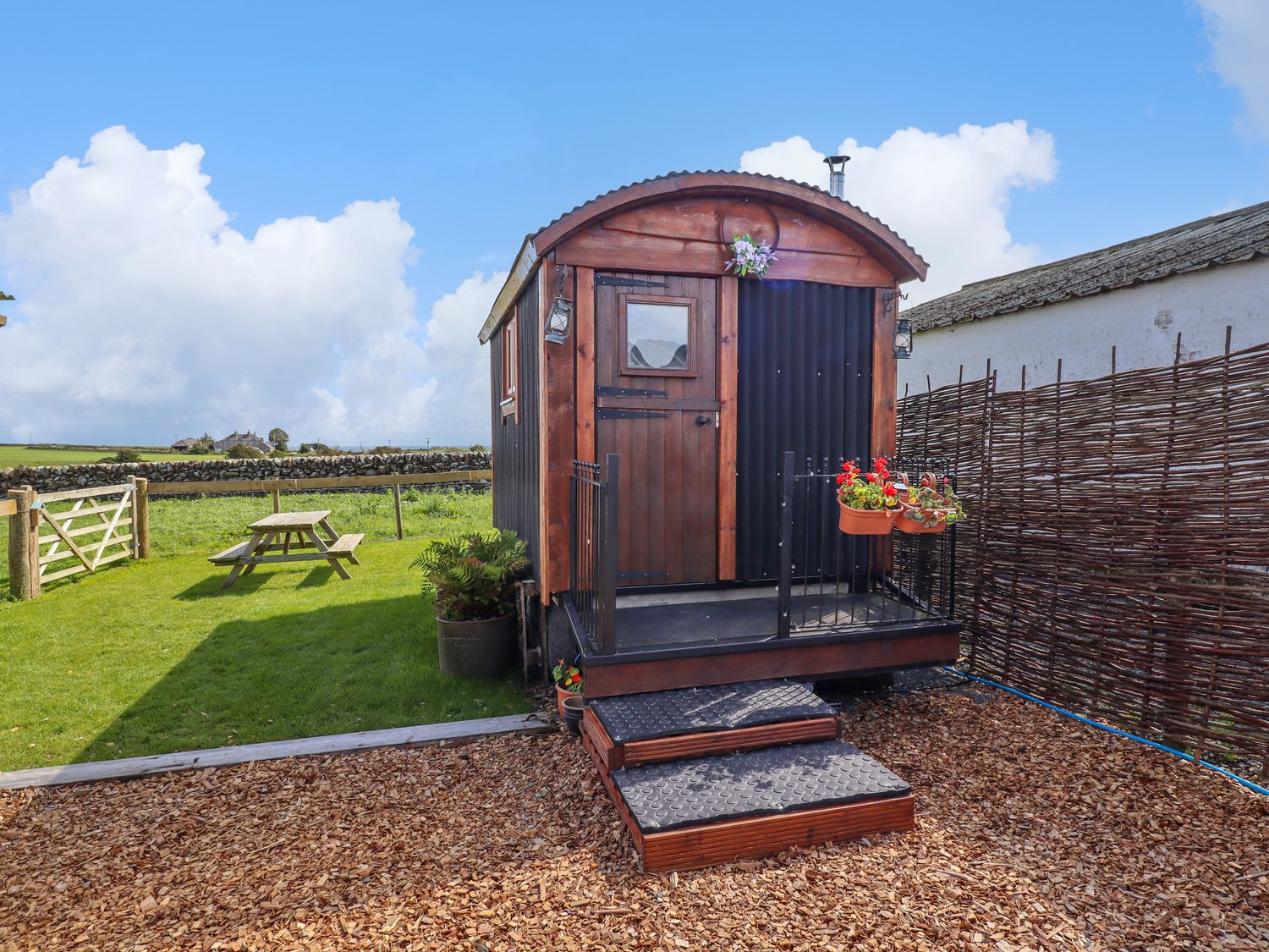 A small wooden cabin with steps and a fenced porch next to a grassy area with a picnic table at The Black Sheep in Whithorn