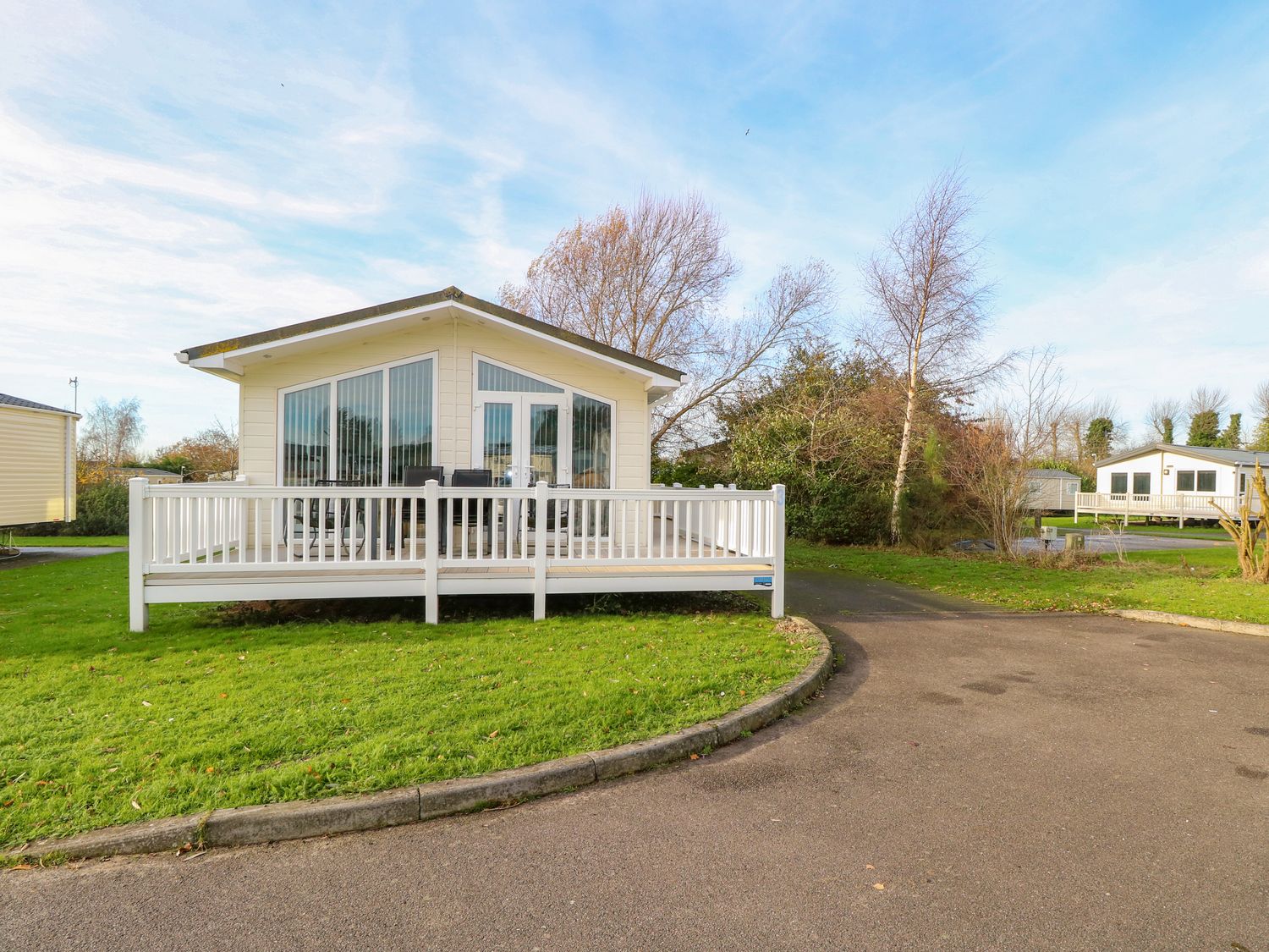 A small house with a white deck and railing in front of a curved road and grass at 3 Bure Close in Burgh Castle