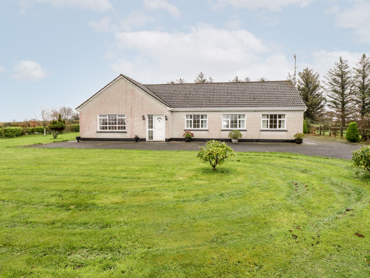 A one-story house with a tiled roof and multiple windows on a lawn with small bushes at Dromore West Cottage in Dromore West County Sligo