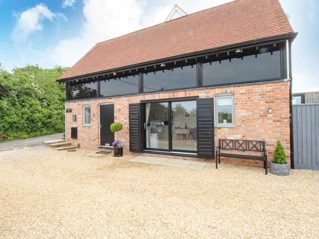 A brick house with black doors and windows a bench and potted plants outside at Meadow View Barn in Bere Regis