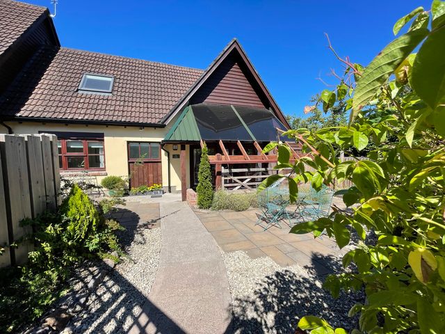 A house with a tiled roof and front garden with patio furniture at The Forge in Shipham