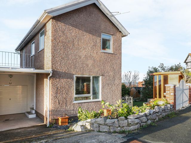 An exterior view of a two-story house with a garage and garden area bordered by stone wall at Bay View House in Colwyn Bay