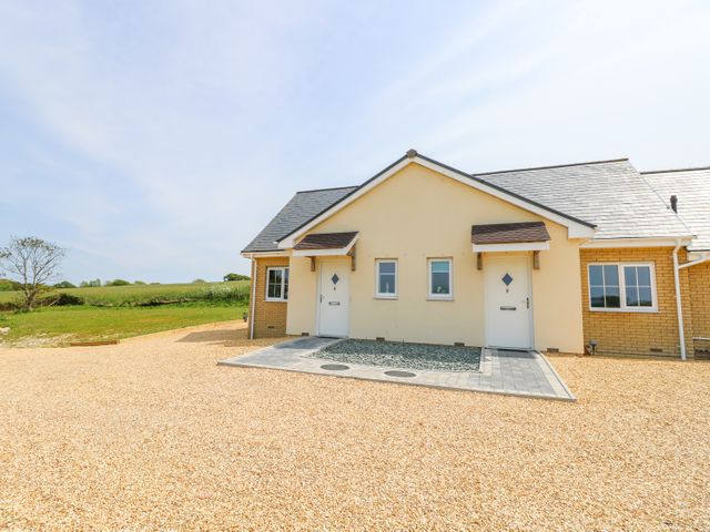 A semi detached single story house with two white doors and small windows on a gravel driveway at 6 Yarmouth Cottages Norton Green near Freshwater