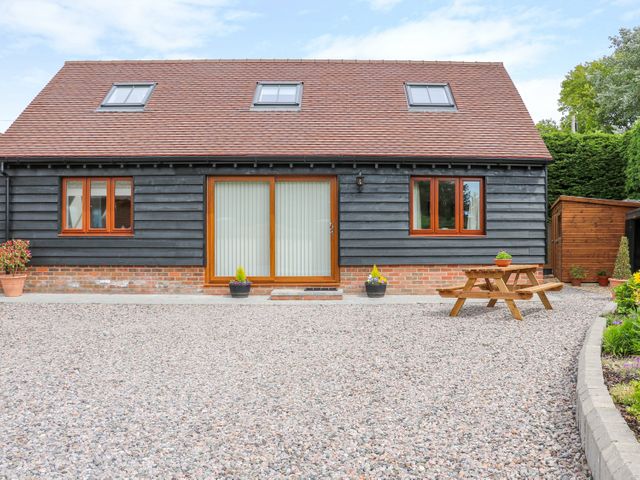 A house with black wooden siding and a red tiled roof with skylights a gravel yard a wooden picnic table and potted plants at Thistledown Cottage in Chidham near Bosham