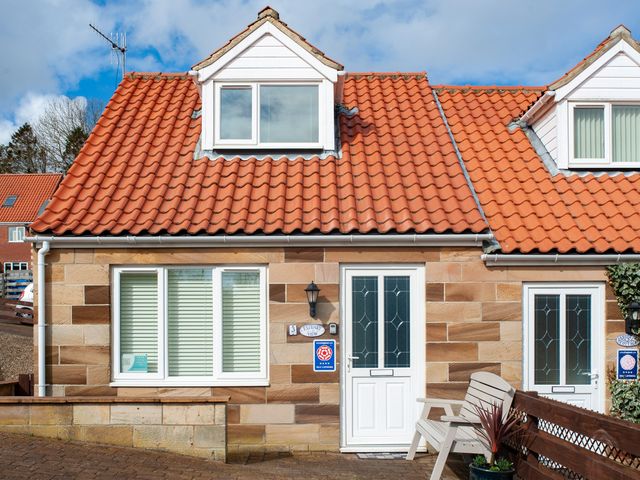 A cottage with red tile roof white doors and windows and a wooden bench outside at Estuary View in Whitby