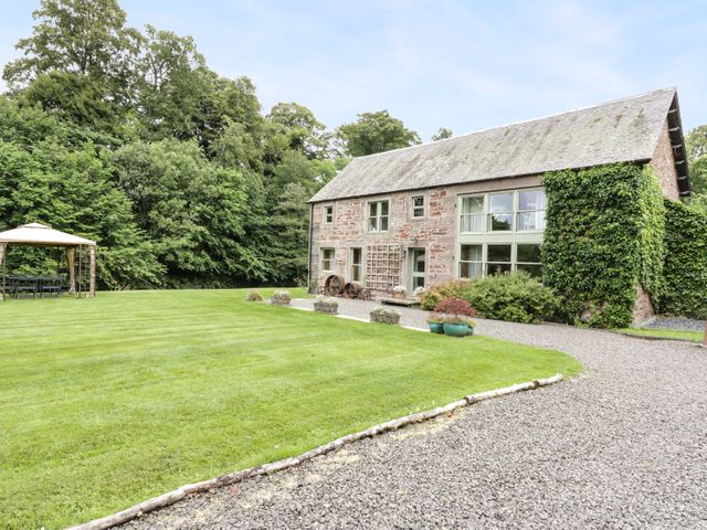 A stone house with large windows surrounded by a lawn and trees at Cardean Mill in Blairgowrie
