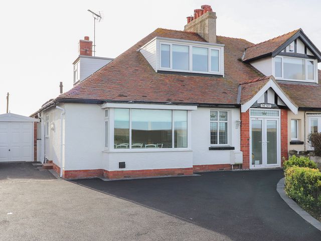 A white semi detached house with a tiled roof a driveway and a garage at The Yatt in Rhos On Sea