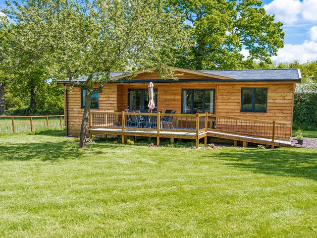 A wooden cabin with a deck and outdoor furniture surrounded by grass and trees at Top Style Orchard in Hallow