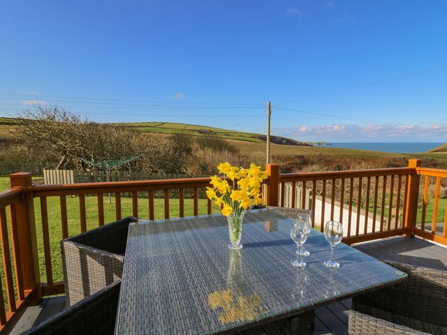 An outdoor patio with a glass table and wicker chairs overlooking a grassy field and the sea at Beudy in Mwnt Cardigan Ceredigion