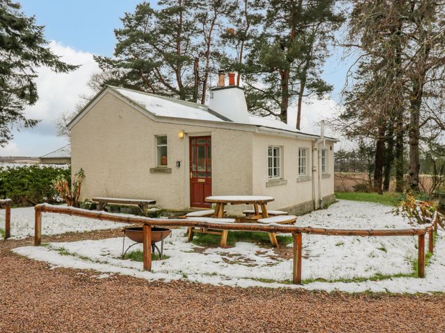 A small house with a red door a picnic table and a fire pit outside with some snow on the ground at The Bungalow in Lhanbryde