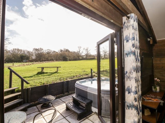 A patio with a hot tub and a small table and chair set opening onto a grassy field at Deer Lodge in Wimborne Minster