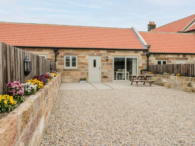 A courtyard with gravel ground and flower beds beside a stone building with a red tiled roof at Shipswheel Cottage at Broadings Farm in Whitby