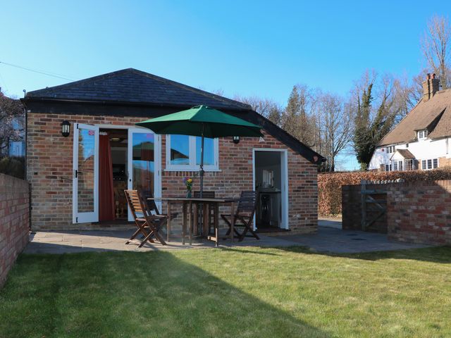 A backyard with green grass a brick house patio with table chairs and green umbrella at The Cowshed in Sedlescombe near Westfield
