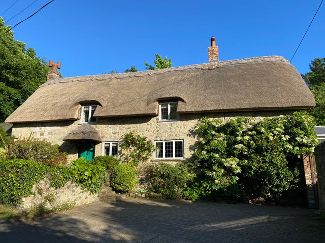 A stone cottage with a thatched roof surrounded by greenery and a paved driveway at Goodalls in Chale near Niton