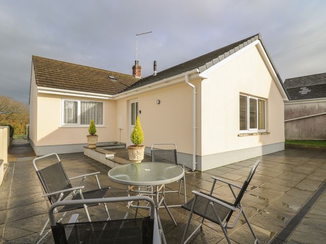 A patio area with glass table and four chairs outside a single story house with cream walls and two potted plants at Avalon in Cilgerran