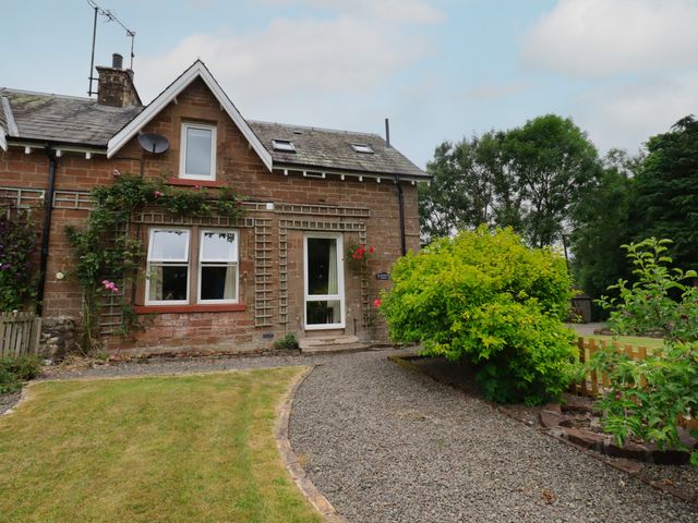 A stone house with a gravel path and green bushes in a garden at Lucy's cottage in Canonbie near Langholm