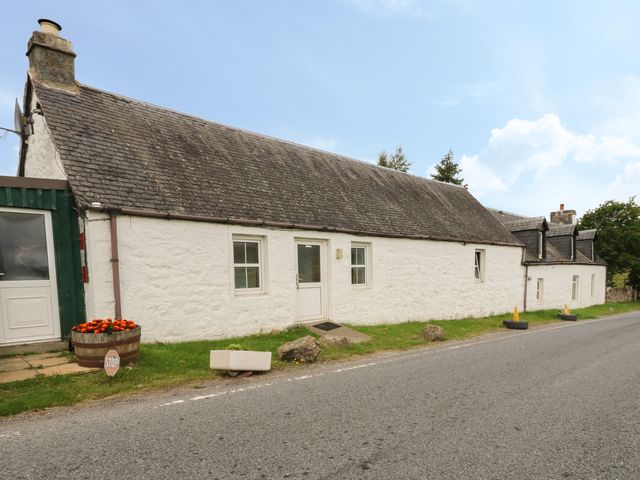 A long white stone cottage beside a road with windows and a door at Osprey Cottage in Laggan