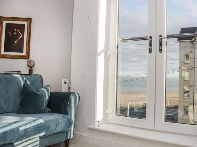 A blue couch with a pillow near a window showing a beach and building at Beach House in Colwyn Bay