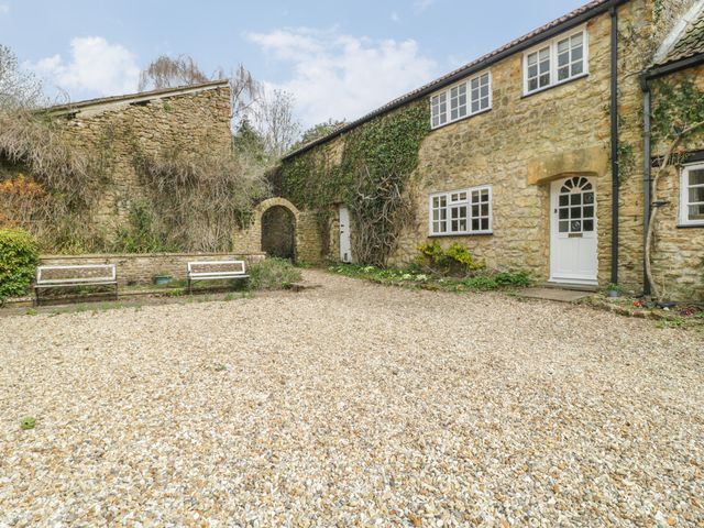 A stone cottage with white doors and windows with a gravel courtyard and benches at Jasmine Cottage in South Perrott near Mosterton