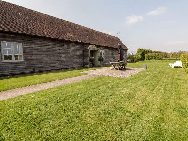A wooden building with a grassy lawn patio table with umbrella and chairs and two white lounge chairs at Jasmine in Wittersham Kent