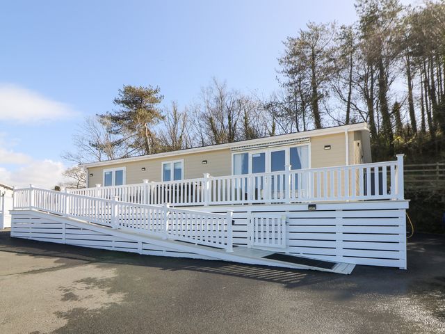 A beige mobile home with white railings and a ramp in front of trees at McAuliffe Lodge in Borth