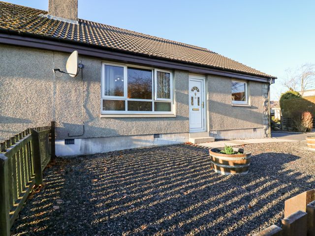 Exterior view of a single-story house with a gravel front yard two wooden planters a white front door and a satellite dish at 10 Annesley Park in Torphins