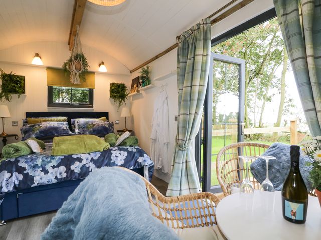 A bedroom with a double bed and floral bedding next to a table with two chairs by a glass door at High Rigg Shepherd's Sunset in Brampton Cumbria