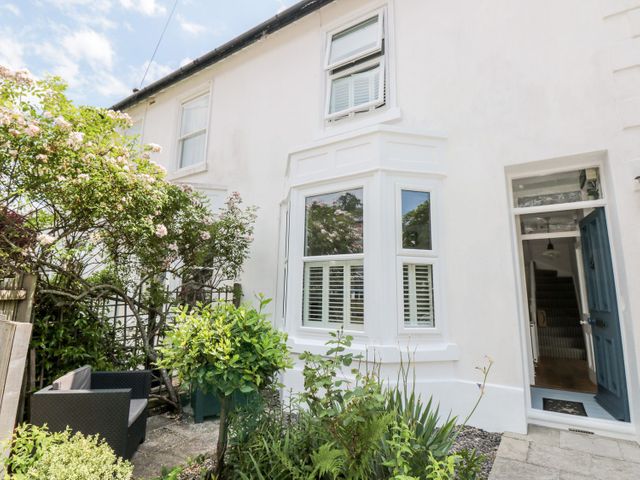 A front garden with outdoor seating and plants in front of a white house with a blue door at Bay Tree Cottage Dartmouth