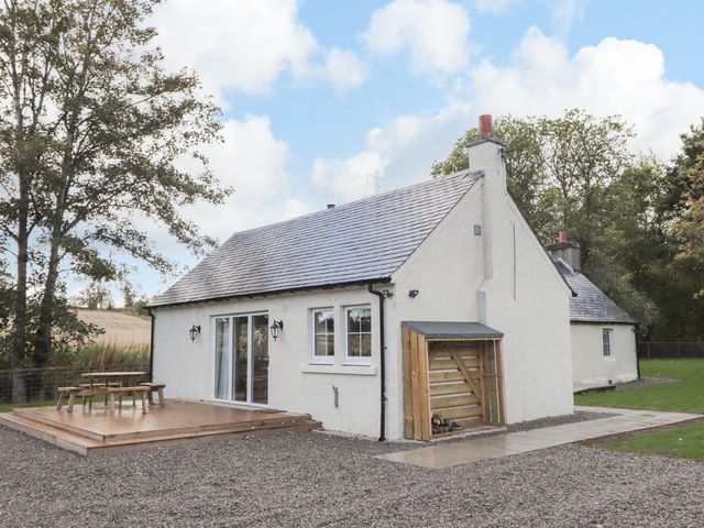 A white house with a wooden deck and picnic table surrounded by gravel and grass at Bonnach in Muir Of Ord