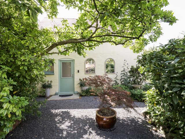 A garden area with gravel path plants in pots and a green door on a white brick building at The Old Post Office Barn in Welland