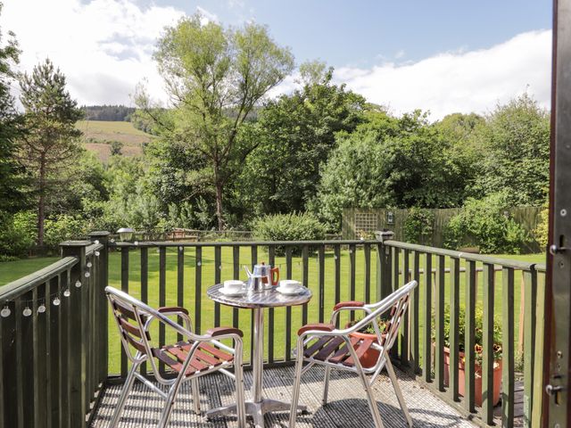 A balcony with two chairs and a metal table with cups and a kettle overlooking a green garden and trees at Iola in Milton near Drumnadrochit Loch Ness
