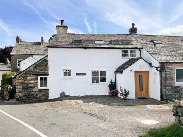 A white stone cottage with a wooden door and multiple windows at Jacky Garth Cottage in Keswick