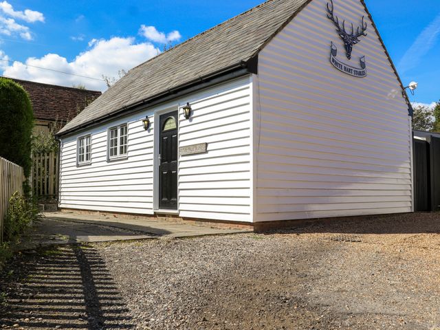 A white wooden building with a black door and windows under a sloped roof at White Hart Stables in Catsfield