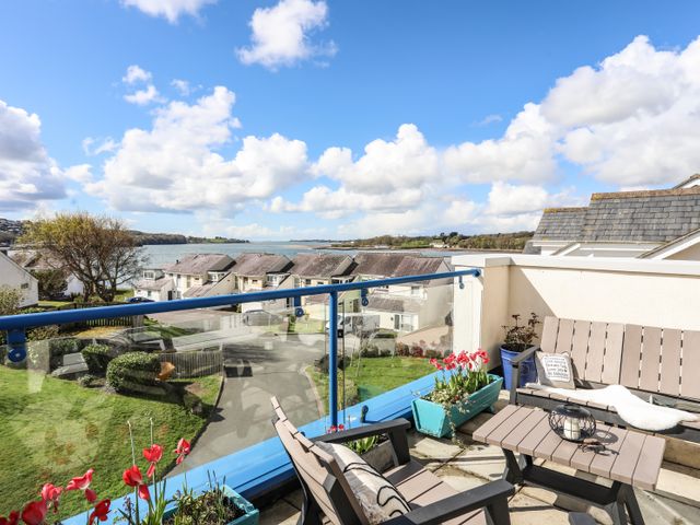 A balcony with outdoor seating and flower pots overlooking houses and water at Menai View in Y Felinheli