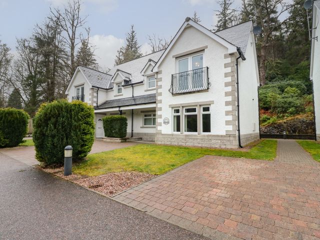 A white two-story house with a paved driveway and bushes in front surrounded by trees at 4 River Court in Invergarry