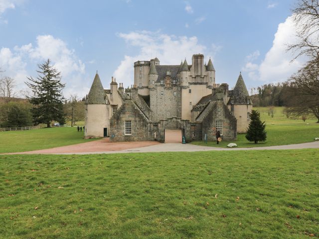 A stone castle with multiple turrets and chimneys surrounded by grass and trees at East Wing - Castle Fraser in Kemnay