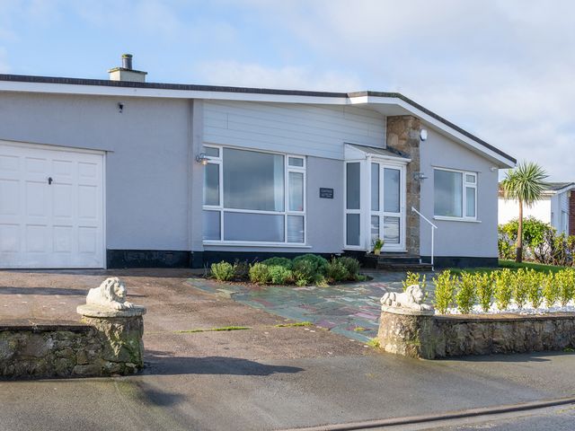 A single-story house with a garage and plants in the front garden at Cartref in Benllech