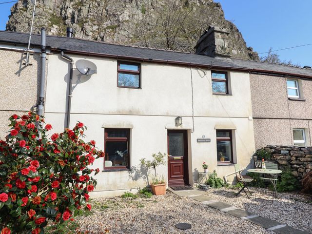 A stone house exterior with a red door red flowers gravel pathway and outdoor table at Bridgeway House in Blaenau Ffestiniog