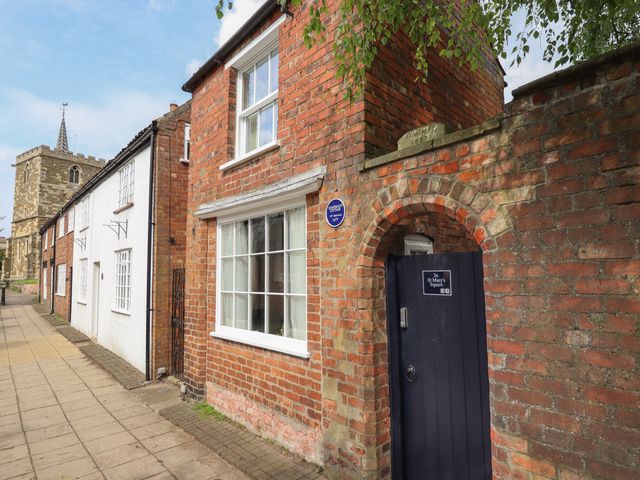A brick house with a black gate and a sign reading 3a St Marys Square next to a church tower at Hangmans cottage in Horncastle