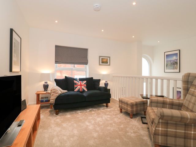 A living room with a dark sofa with a union jack pillow a plaid armchair and ottoman a television on a wooden stand and framed pictures on white walls at Flat 2 in Bournemouth