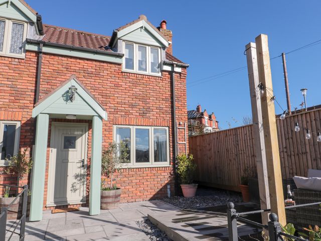 Front exterior of a brick house with a pale green door canopy and patio area at Rosemary Cottage in Briggswath near Sleights