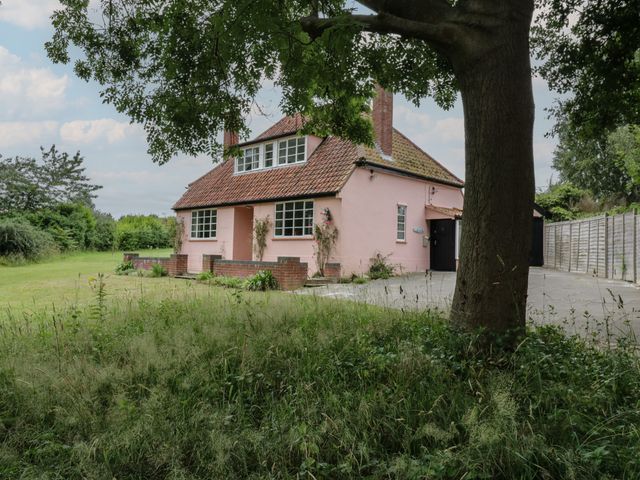 A pink house with a tiled roof behind a large tree and a grassy yard at Ash Tree Cottage Aldringham