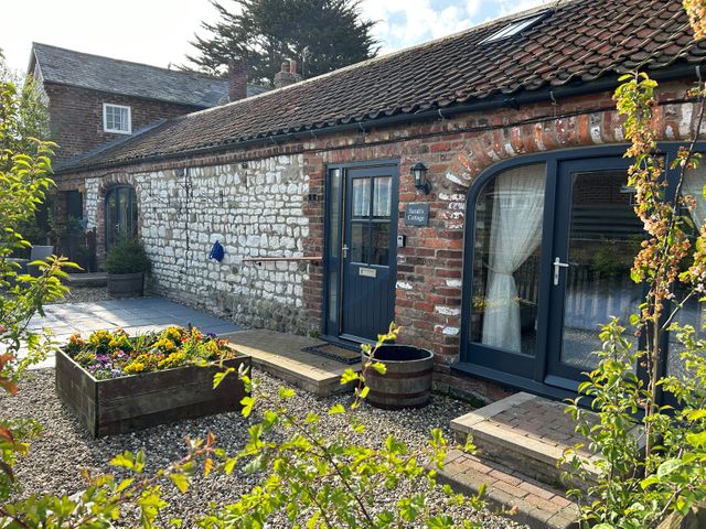 An exterior view of a cottage with stone and brick walls a wooden planter with flowers and a gravel pathway at Sarah's Cottage in Flamborough