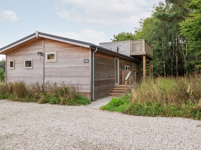 A wooden cabin with a raised balcony surrounded by gravel and greenery at 9 Meadow Retreat in Dobwalls