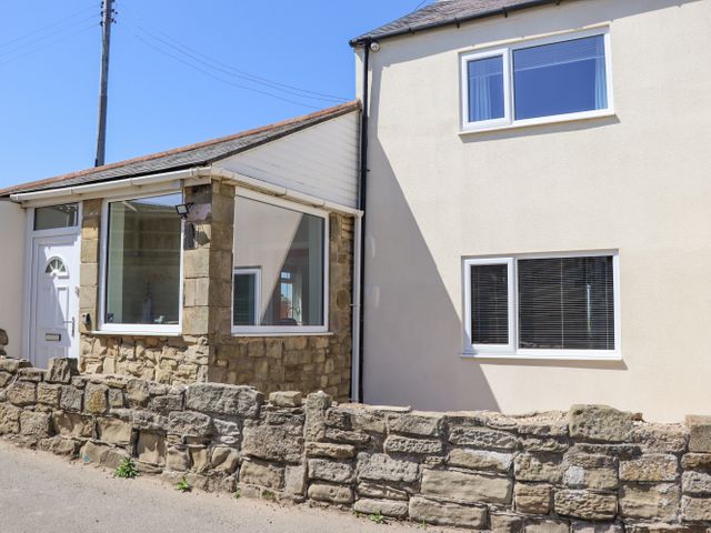The exterior of a house with stone and white walls windows and a low stone wall by the roadside at Island View in Amble