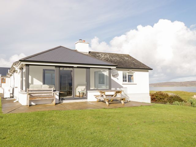 A white house with a tiled roof patio wooden bench and picnic table on green grass at Seacrest in Ballyconneely County Galway