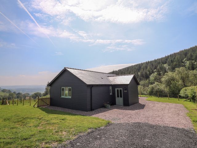 A single-story dark wooden house with a gravel driveway surrounded by grass and trees at Ystrad Wen in Llysdinam near Newbridge-On-Wye