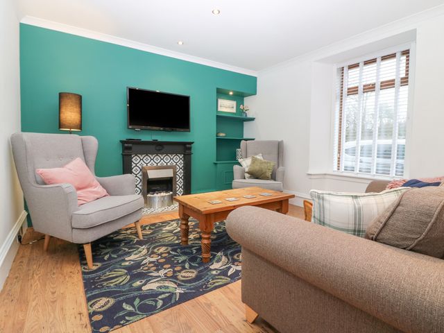 A living room with two armchairs a sofa a wooden coffee table a patterned rug a wall-mounted tv and a window with blinds at 16 Main Street Newburgh near Ellon