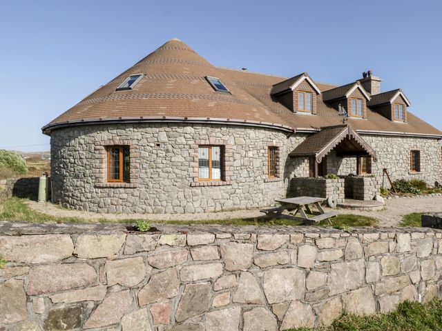 A stone house with a conical roof and wooden windows behind a stone wall at Baile Na Cille on Lettermullen County Galway